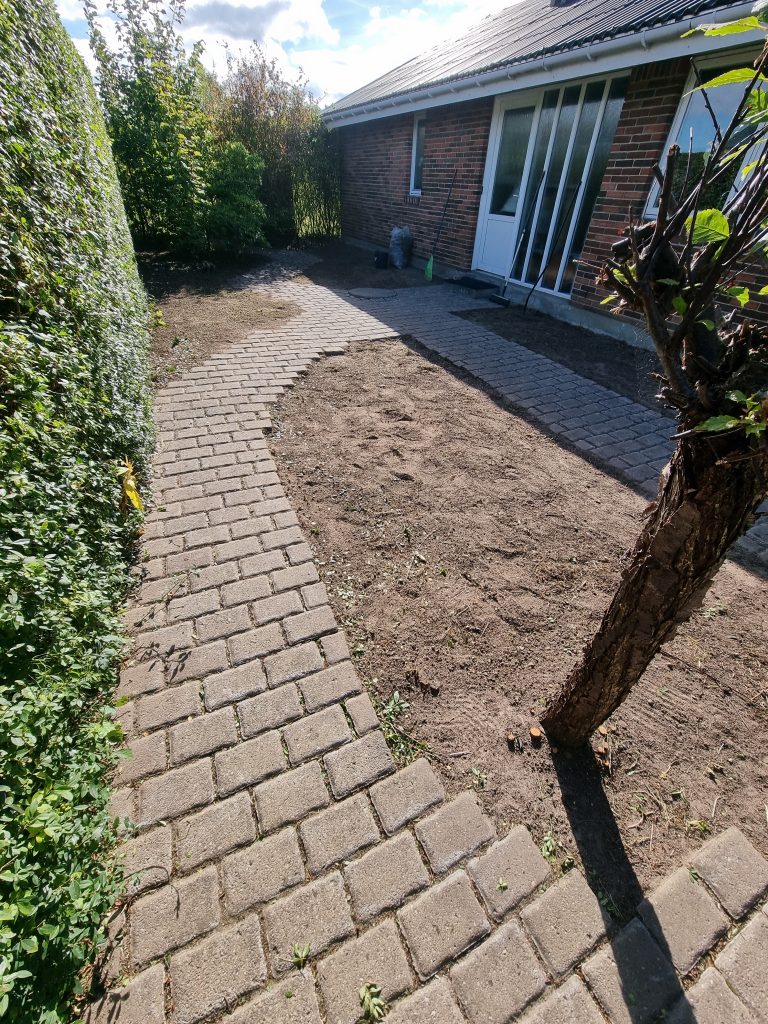 En ren og pæn flisesti efter professionel ukrudtsbekæmpelse og havepleje, hvor alle bede er luget og jorden er klargjort.